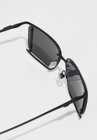 Black sunglasses with rectangular lenses, thin metal frame, rubber nose pads, and dark tinted lenses. Lightweight design, minimal embellishments.