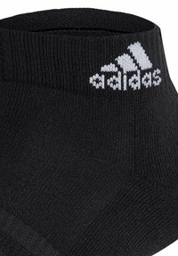 Chaussette de sport noire avec une texture côtelée, affichant un logo Adidas blanc en haut et un design à coupe basse qui se situe au-dessus de la cheville.