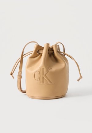 Tan leather bucket bag with drawstring closure and adjustable shoulder strap, embossed with large "cK" logo on front.