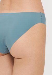 Blue bikini bottom made from smooth fabric, featuring a low-rise design and minimal coverage. Seam detailing on the sides.