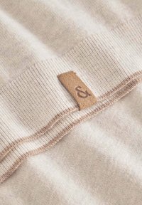 Beiger Strickstoff mit strukturierter Oberfläche und feinem Rippenabschluss, versehen mit einem kleinen braunen Lederetikett mit eingeprägtem "&".