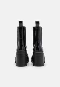 Botas de tobillo de charol negro con un tacón chunky, que presentan paneles laterales elásticos y una lengüeta para facilitar el calzado. Textura suave y diseño elegante.