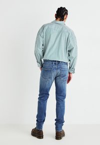Grönrandig skjorta med långa ärmar och puffärmar, kombinerad med blå jeans. Bruna snörkängor med kraftiga sulor. Enkelt mönster, avslappnad passform.