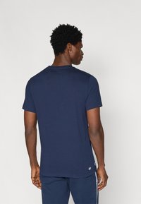 Σκούρο ναυτικό μπλουζάκι κοντομάνικο με στρογγυλή λαιμόκοψη, λεία υφή και ένα μικρό λογότυπο κοντά στο στρίφωμα. Απλός, κλασικός σχεδιασμός.