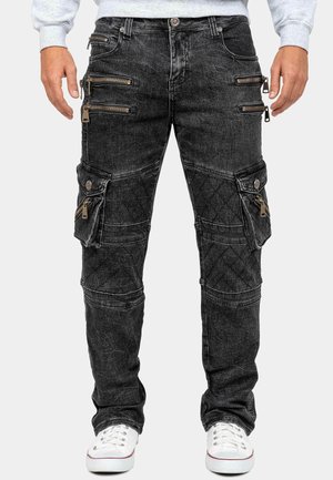 Schwarze Cargo-Jeans mit mehreren Reißverschlusstaschen und gesteppte Kniepolster, kombiniert mit weißen Sneakern und einem hellgrauen Sweatshirt.