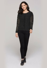 Schwarzer Strickpullover mit einem strukturierten, offenen Strickmuster, rundem Halsausschnitt und langen Ärmeln. Kombiniert mit schwarzen, schmalen Hosen und Sneakers.
