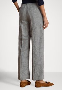 Γκρι ψηλόμεσο παντελόνι με καρό σχέδιο και άνετη εφαρμογή, με πίσω τσέπες και ίσια γραμμή στο πόδι. Τα καφέ σουέντ μοκασίνια ολοκληρώνουν την εμφάνιση.