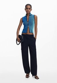 Blå ombré ærmeløs top med lodret ribstrik og lynlås foran, kombineret med sorte cargobukser med vide ben og sort håndtaske.