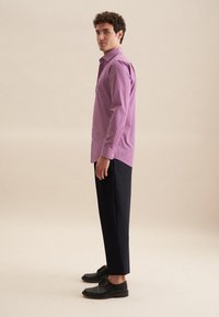 Una camicia a fantasia rosa con colletto a bottoni, abbinata a pantaloni scuri e scarpe nere. Tessuto morbido e vestibilità su misura.