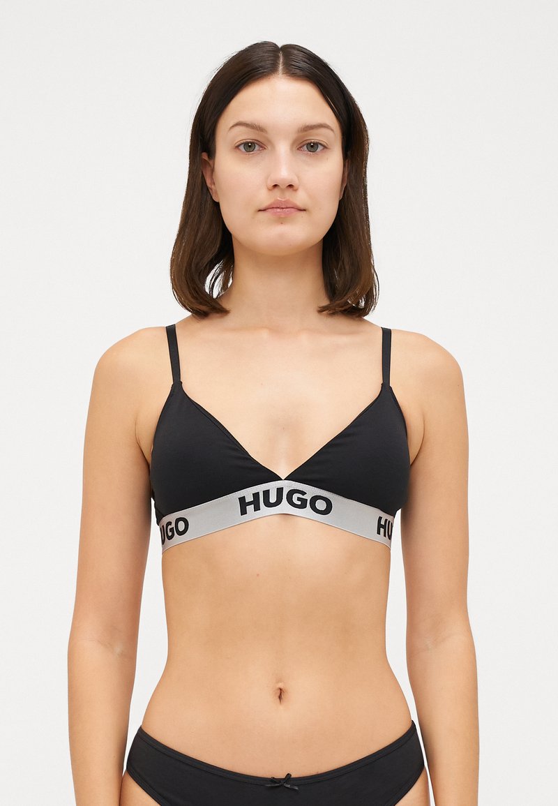 Μαύρο μπραλέτ με τριγωνικό σχήμα, φτιαγμένο από λείο ύφασμα. Διαθέτει μια φαρδιά γκρι ζώνη με την ένδειξη "HUGO" τυπωμένη σε μαύρο στο κάτω μέρος.