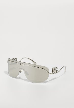 Lunettes de soleil avec une esthétique élégante, un cadre argenté fin, de grandes lentilles teintées en gris et un logo distinctif sur les branches, présentant un design incurvé.