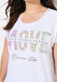 T-shirt en coton blanc à manches courtes, avec un texte en strass multicolores : "AGIS FAIS QUE LES CHOSES SE PRODUISENT" et "N'arrête jamais."