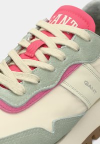 Κοντινό πλάνο αθλητικού παπουτσιού GANT με μπεζ κορδόνια, λεπτομέρειες από σουέντ σε ανοιχτό πράσινο, ροζ αποχρώσεις και λευκή βάση με ραφές.