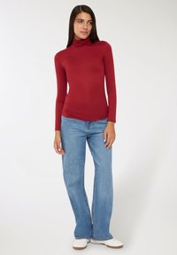 Bordowy sweter z golfem i długimi rękawami, zestawiony z jasnoniebieskimi dżinsami w dzwony i białymi butami. Gładka faktura, dopasowany krój, podstawowy wzór.