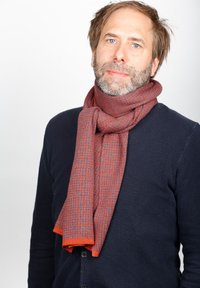 Red and blue patterned scarf made of soft fabric, draped around the neck. Accented with an orange trim. Worn with a navy sweater.