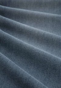 Ddenim-Stoff in Dunkelblau, der eine glatte Textur mit weichen Drapierungen und einem subtilen, gleichmäßigen Webmuster aufweist. Keine sichtbaren Hardware oder Akzente.