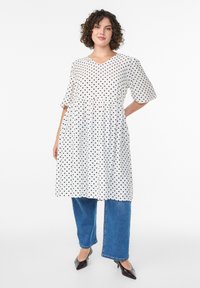 Valge kleit mustade täppidega, V-kaelusega, lühikeste varrukatega, kogutud vöökoht. Kombineeritud siniste laia säärega teksade ja mustade terava ninaga kontsadega.