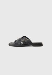 Sandales noires à semelle plate en cuir texturé, avec des sangles croisées et une semelle en caoutchouc, agrémentées d'un logo de marque discret.
