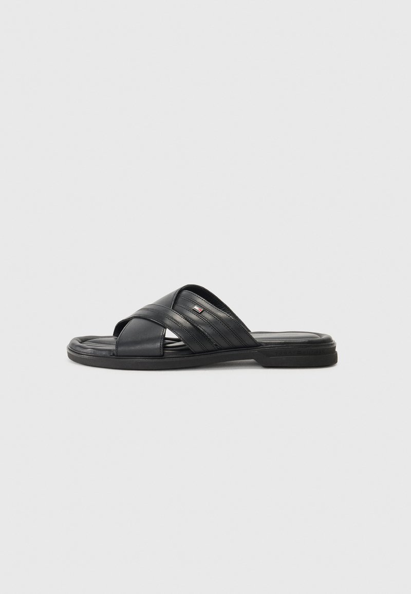Sandales noires à semelle plate en cuir texturé, avec des sangles croisées et une semelle en caoutchouc, agrémentées d'un logo de marque discret.