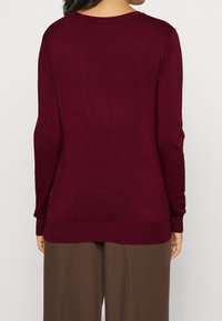 Burgunderfarbener Strickpullover mit langen Ärmeln, rundem Halsausschnitt und gerippten Bündchen und Saum. Glatte Textur mit minimalen Details.