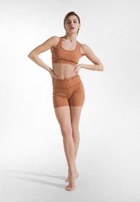 Conjunto de ropa deportiva naranja, que incluye un top corto sin mangas y pantalones cortos de talle alto con una banda con logo. Textura suave, diseño ajustado y acabado sin costuras.