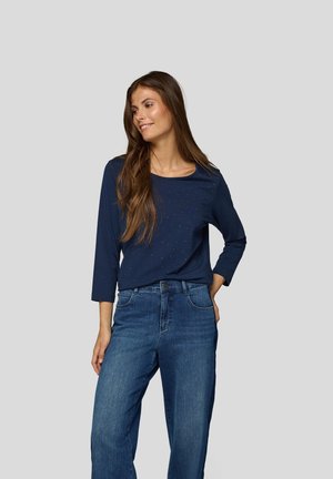 Marineblaue Langarmbluse mit einem Rundhalsausschnitt und feinem Punktmuster, kombiniert mit hellblauen Schlagjeans, die über traditionelle Taschen verfügen.