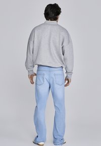 Felpa grigia con colletto alto e spalle cadenti, abbinata a jeans azzurri chiari con un classico design a cinque tasche.