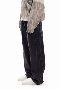 Μαύρο τζιν παντελόνι σε μεγάλο μέγεθος με ίσια γραμμή, με ορατές ραφές, φορεμένο με λευκά παπούτσια χωρίς κορδόνια.