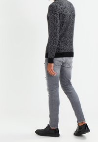 Schwarzer und weißer Heringbone-Muster-Pullover mit Rundhalsausschnitt, getragen mit hellgrauen, abgenutzten Jeans und schwarzen Sneakers. Rückansicht.