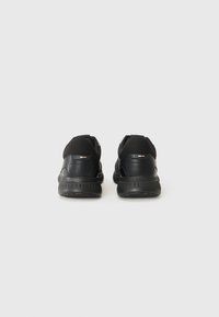 Zapatillas deportivas negras con un upper de malla y sintético, puntera redondeada, suela acolchada y un detalle de marca sutil en el talón.
