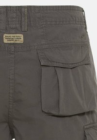 Graue Cargo-Shorts mit entspannter Passform, die mehrere seitliche Taschen, genähte Details und ein gewebtes Etikett mit der Aufschrift "FÜR TÄGLICHE ABENTEUER GEMACHT" aufweisen.