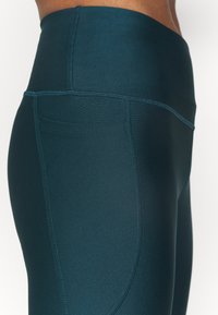 Turkusowe legginsy z wysokim stanem, wykonane z elastycznego materiału, z szerokim pasem i boczną kieszenią, z płaskimi szwami.