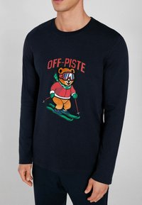 Námořnické triko s dlouhým rukávem s potiskem kresleného medvěda, který lyžuje, a nápisem "OFF-PISTE" v červené barvě. Měkká tkanina s kulatým výstřihem a uvolněným střihem.