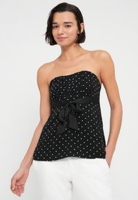 Svart stroppeløs topp med hvite polkadotter, rynket overdel og et knytt stoffbelte i midjen. Jevn tekstur, flytende design.