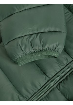 Veste verte rembourrée avec des poignets côtelés, une bande élastique marquée et une fermeture éclair sur le côté. Le matériau semble lisse avec un léger éclat.