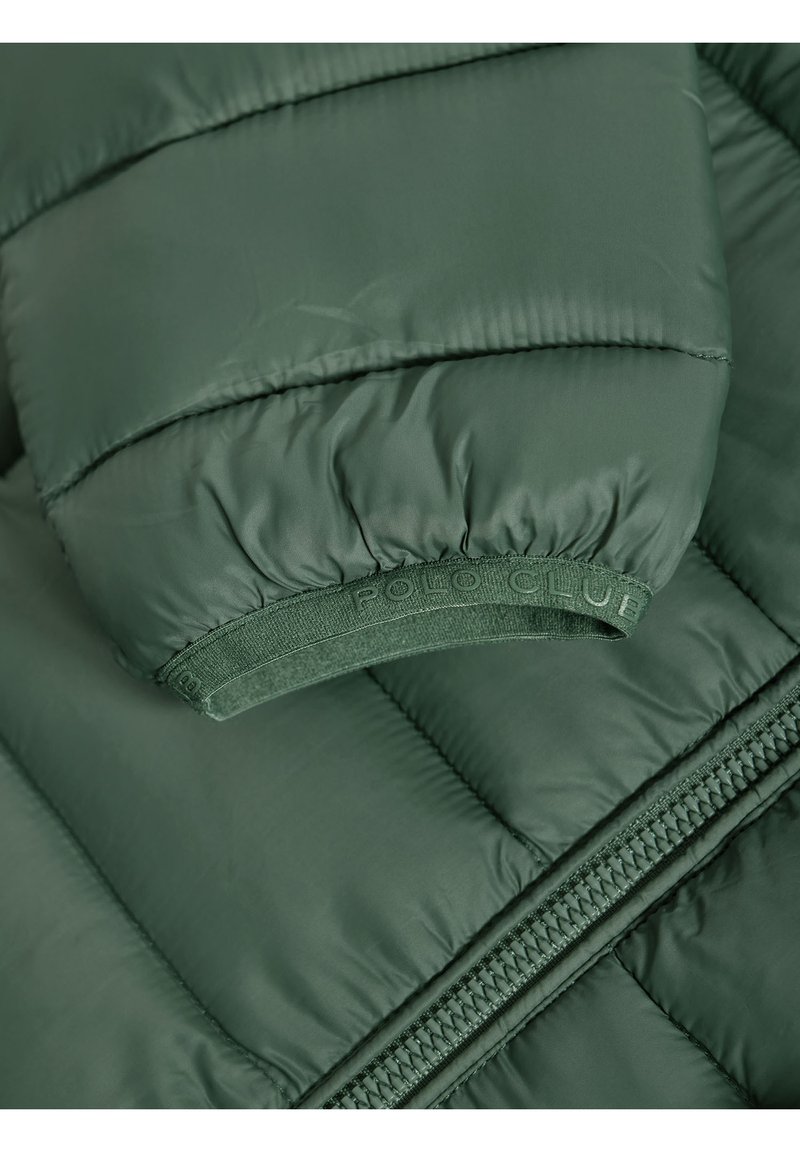 Vadderad grön jacka med ribbad mudd, märkeselastiskt band och siddragkedja. Materialet verkar slätt med en lätt lyster.