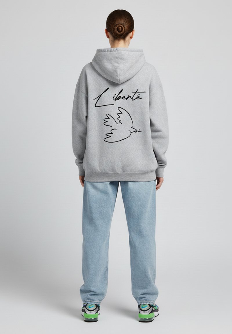Felpa grigia con un contorno nero di una colomba e la parola "Liberté" sulla schiena; abbinata a pantaloni azzurri e sneakers.