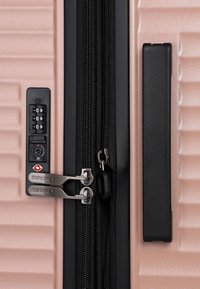 Růžový tvrdý kufr s černou rukojetí, dvojitými zipy označenými "SURI FREY" a integrovaným zámkem TSA s kombinací.