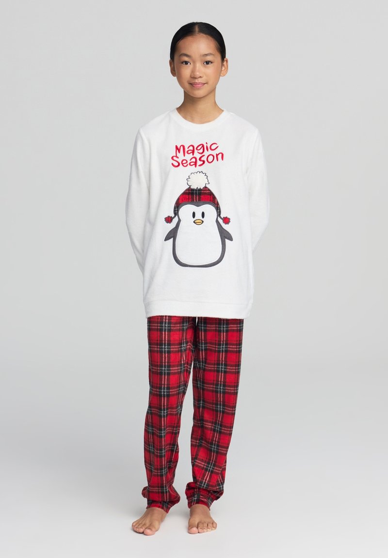 Biała bluzka z długim rękawem z grafiką pingwina i czerwonym napisem "Magic Season", w zestawie z czerwonymi, w kratkę flanelowymi spodniami z czarnymi akcentami.