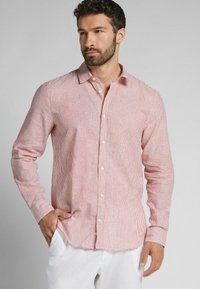 Rot-weiß gestreiftes Langarmhemd mit Button-Down-Kragen, locker geschnitten und mit gefalteten Ärmeln, getragen zu hellen Hosen.
