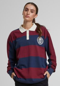 Dlhý rukáv polo tričko s vínovými a námorníckymi pruhmi, s bielym golierom a vyšitým logom na hrudi. Mäkka, priedušná tkanina.