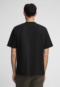 Camiseta negra de manga corta hecha de una tela suave, con cuello redondo y un corte relajado. La vista trasera muestra líneas limpias y sin detalles visibles.