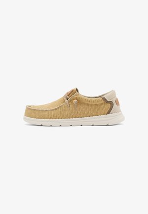 Zapato casual sin cordones con parte superior de tela beige tejida, suela blanca y detalles en marrón claro, diseñado para comodidad y uso diario.