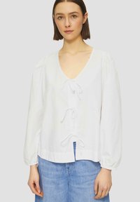 Weiße Bluse mit langen Ärmeln und V-Ausschnitt, ausgestattet mit drei vorderen Bindebändern und gerüschten Ärmeln. Strukturierter Stoff, fließendes Design und bequeme Passform.