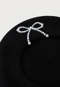 Μαύρο μπερέ με διακοσμητική κορδέλα φτιαγμένη από λευκές πέρλες σε διάφορα μεγέθη τοποθετημένες στην κορυφή.
