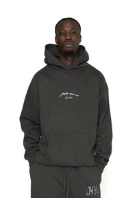 Hoodie in Dunkelgrau mit einer Fronttasche und weißer Logostickerei. Hergestellt aus weichem Stoff mit lockerer Passform.