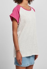 T-shirt z krótkim rękawem o szarym ciele i różowych rękawach raglanowych. Wykonany z miękkiego materiału, charakteryzujący się okrągłym dekoltem i luźnym krojem.