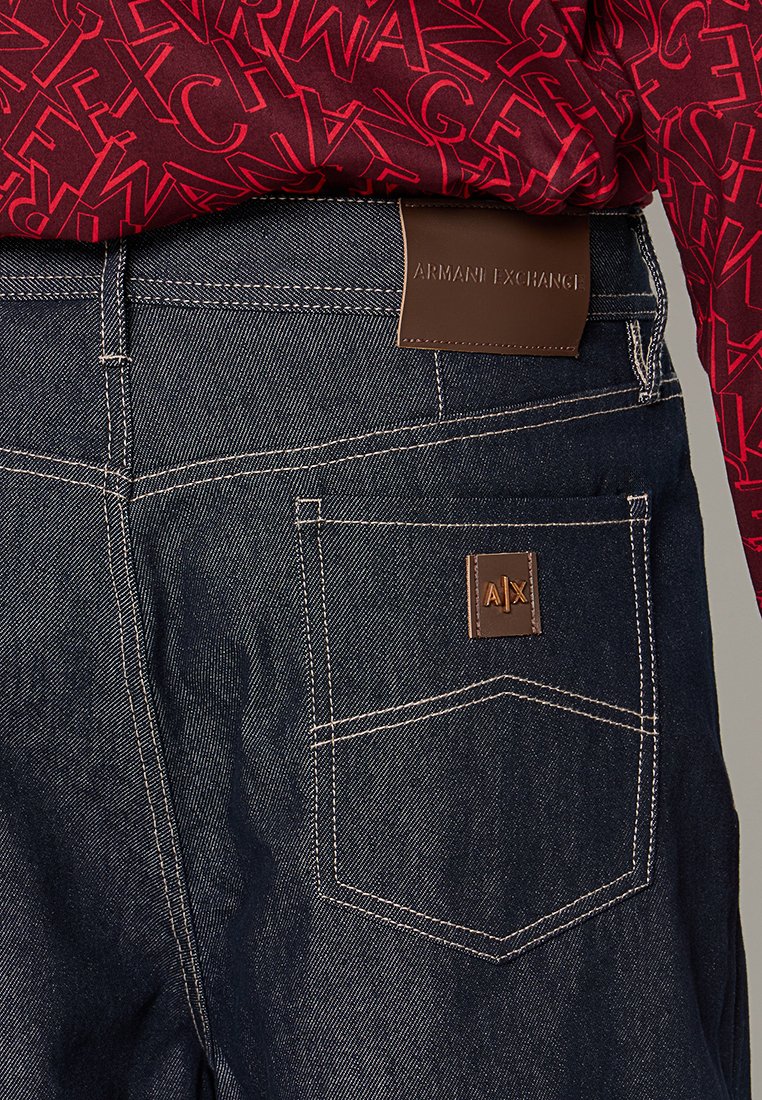 Dunkelblaue Jeans aus Denim verfügen über ein braunes Lederetikett mit "ARMANI EXCHANGE." Sichtbare Nähte und das Taschendesign heben funktionale Details hervor.