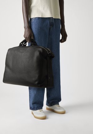 Sac en cuir noir avec une surface texturée, de forme arrondie, deux poignées supérieures et deux zips. Présente un design simple et épuré.