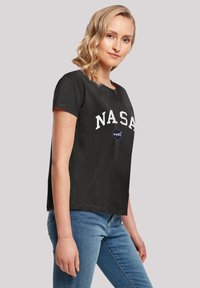 Black cotton t-shirt with white “NASA” lettering and circular logo on the chest, featuring short sleeves and a relaxed fit.